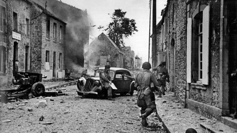 在法国主要港口城市瑟堡南部一个村庄的街道上，被遗弃的报废汽车。在这张图片中，美国第82空降师的士兵小心翼翼地穿过该地区。