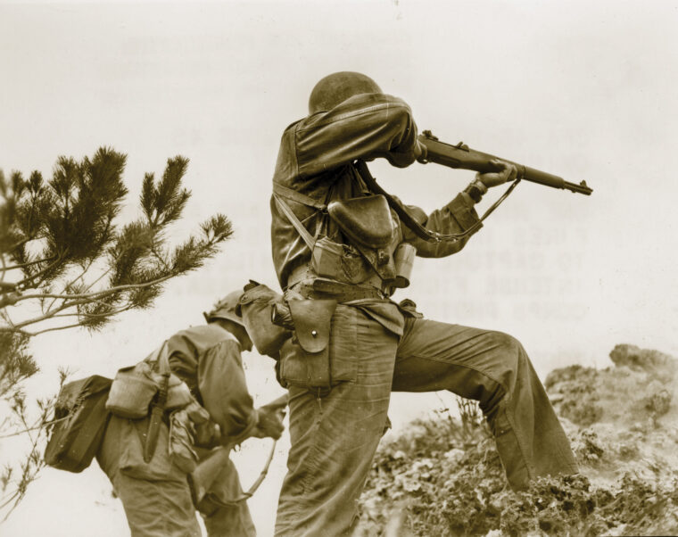 两名美国第96步兵师的士兵在冲绳岛上与顽固的日本守军交战。可以看到其中一人用他的M-1加兰德步枪向远处的目标射击，而另一人正在给武器上膛。冲绳的血战持续了82天。