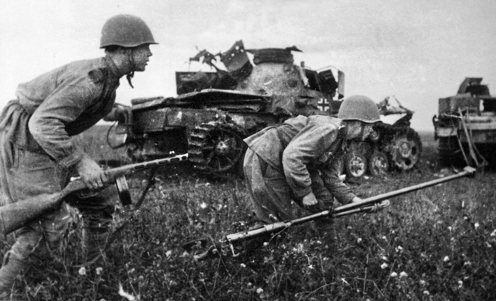 苏军步兵蹲着冲过德国坦克残破的残骸。右边的士兵拿着一支重型反坦克步枪，这种步枪对德国的中型和重型坦克毫无效果。