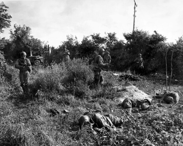 美国伞兵,与他们的武器准备好了,提前谨慎通过跟随附近,散落着战友的尸体,由德国神枪手摘的,1944年6月14日。