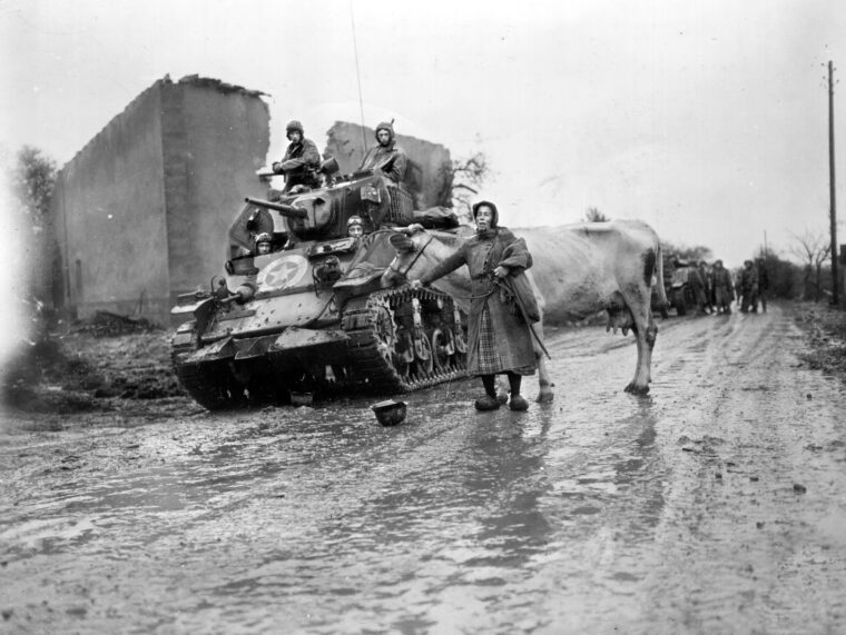 坦克乘员的第二骑兵团耐心地等待一个法国女人和她的牛穿过雨水浸透的道路附近的吕内维尔在1944年的秋天。团是第四装甲师的一个组成部分,发挥了关键作用破坏德国试图切断第四装甲和摧毁它。一个废弃的德国头盔位于巷道。