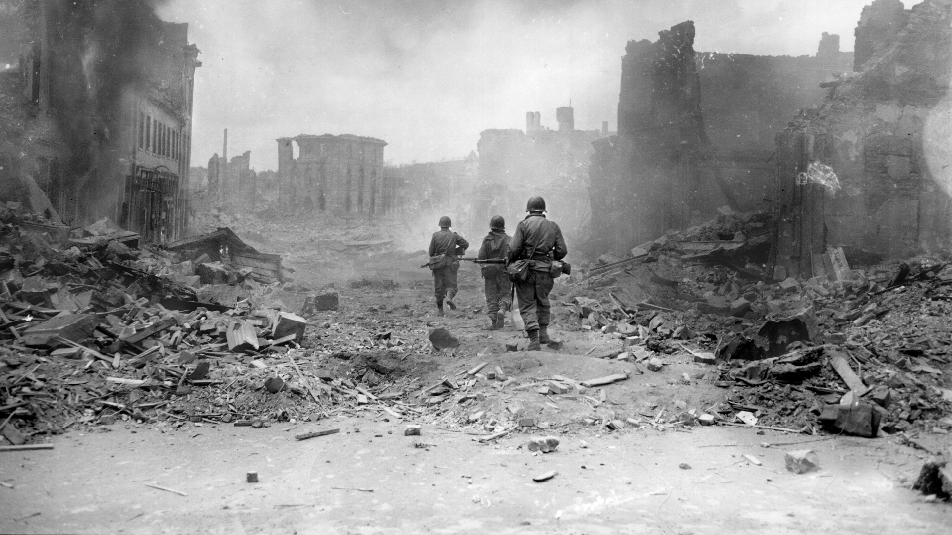 1944年3月20日，德国茨威布鲁肯，步兵第30团第3师的士兵们小心翼翼地穿过废墟。在这座被摧毁的城市里，一些大火仍在燃烧。