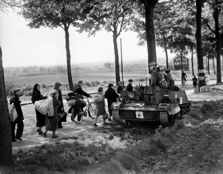 1940年春天，一辆英国布伦机枪运输车经过一长列逃离德军猛攻的法国难民。英国士兵正向比利时边境进发，试图阻止德军的进攻。
