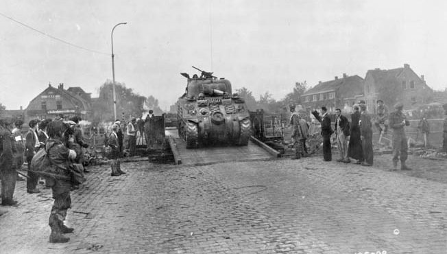一辆英国谢尔曼坦克穿过荷兰威廉敏娜运河，美国101空降师伞兵和荷兰平民在一旁观望。盟军对威廉敏娜运河的控制对地面部队向阿纳姆的英国伞兵挺进至关重要。